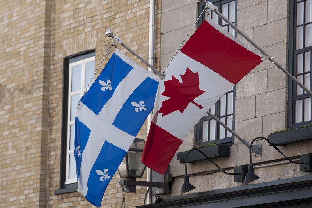 Quebec and Canadian flags displayed side by side on a stone building facade