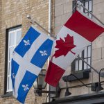 Quebec and Canadian flags displayed side by side on a stone building facade
